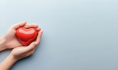 Two hands holding a red heart on a light blue background.