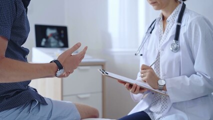 Doctor woman is taking notes on a clipboard while a male patient describes his symptoms in clinic procedure cabinet. Medicine service