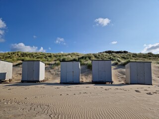
Sandy North Sea beach in Zeeland, the Netherlands. Small white beach storage cabins in a row, in front of the sand dunes