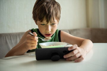 Child boy eats by game. Kid eating and surfing on internet or playing video games on console. Gadget addiction, habit