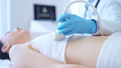 Doctor man, wearing blue medical gloves, is using ultrasound machine to examine internal organs of...
