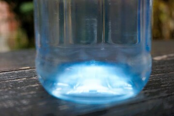 Blaue transparente Glasflasche mit Wasser auf altem grau-braunem Holztisch stehend im Garten am Abend im Sommer