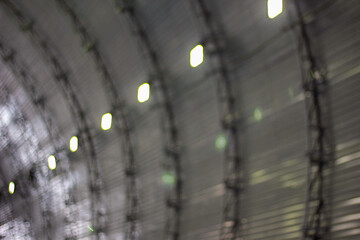 A blurred perspective of an arched, metal-clad interior, where the rows of lights create a rhythmic pattern across the ribbed surface. The softened focus adds a sense of movement and flow to the indus