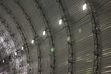 A detailed look at the interior of an arched, metal-clad structure, where evenly spaced lights illuminate the ribbed panels, creating a sense of rhythm and symmetry. The clean lines and structured des