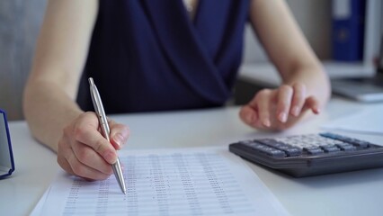 Businesswoman with dark blue dress is using white calculator and taking notes in her office. Taxes and audit in business