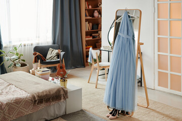 Elegant light blue dress hanging on wooden stand in cozy bedroom with natural decor