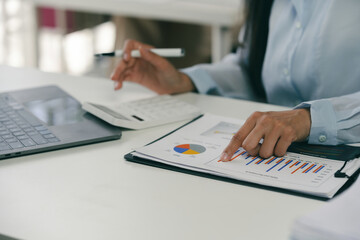 Businesswoman is analyzing financial charts at her desk, using a calculator to assist with her calculations