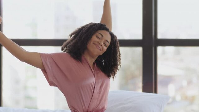 Lazy morning. Young well slept african american woman in pajamas stretching, sitting in bed, waking up, greeting new day