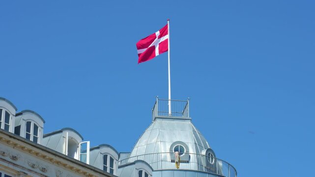 Danish flag is waving on building roof on sunny day against blue sky