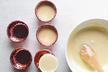 Overhead view of vanilla cupcake batter in pink cupcake liners, cupcake batter in metallic pink cases, process of making cupcakes