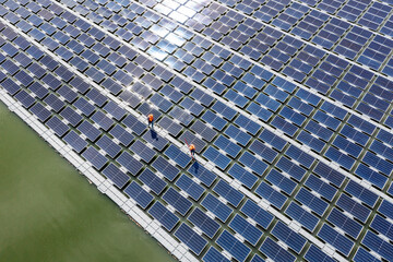Worker cleans floating solar panels on a lake, using a brush and water to maintain the solar cell...