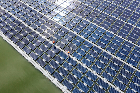 Worker cleans floating solar panels on a lake, using a brush and water to maintain the solar cell platform system.