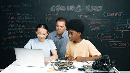 Caucasian teacher pointing at laptop while teaching about engineering code. Instructor working by using laptop while happy highschool student learning and studying programing system. Edification. © InfiniteFlow