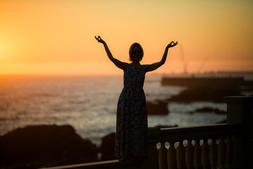 The silhouette of a woman stands on an ocean promenade at twilight.