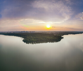 Big lake with green shores in bright sun light and city on horizon, aerial landscape. Recreation concept. Aerial view