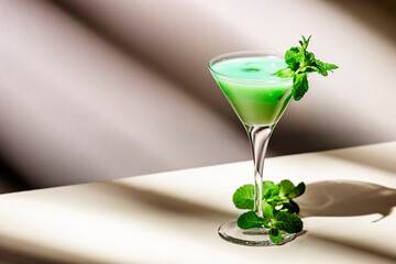 Green alcoholic cocktail drink with liqueur, cream, ice and mint. Beige background, hard ligh