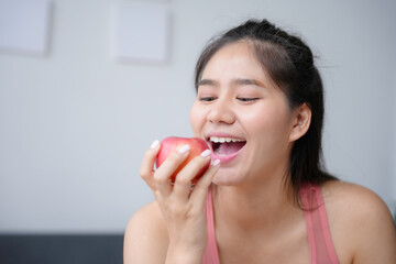 Young woman is happily taking a bite of a red apple, promoting healthy eating habits