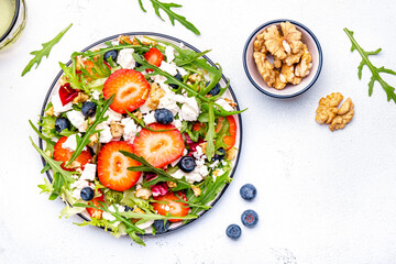Strawberry and feta salad with arugula, lettuce, blueberries, cheese and walnuts, white background, top view