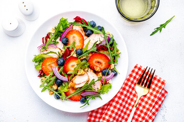 Strawberry and chicken fresh salad with arugula, blueberries, onion and walnuts, white background, top view