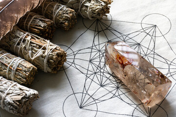 An image of several white sage smudge stick and healing crystal on a sacred geometry grid cloth.