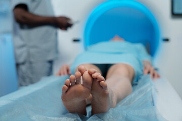 Individual lying on examination table undergoing MRI scanning procedure, medical professional standing by equipment