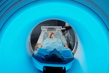 Individual undergoing MRI scan within medical facility while technician supervises procedure from outside