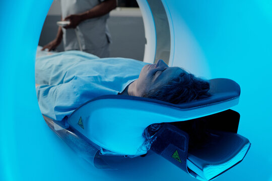 Individual lying on medical imaging table, undergoing an MRI scan inside hospital, with a technician in background readying equipment