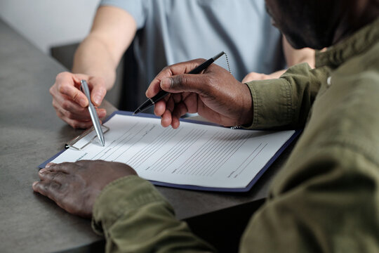 Two people sitting at table, signing important business documents with pen