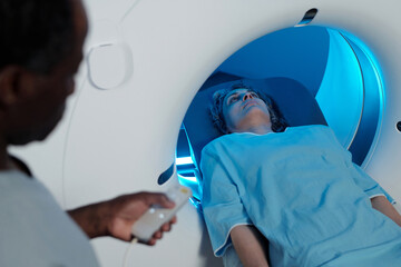 Person lying inside MRI scanner receiving diagnostic imaging with medical personnel operating machine nearby