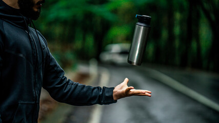 A man throws his thermos into the air. In a deserted forest, a man throws a metal stainless thermos...