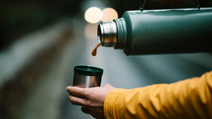 Close-up of man hand pouring coffee from green colored thermos into cup. Photo of metal stainless...