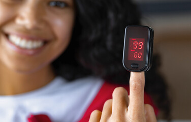 Happy African American woman with portable pulse oximeter on a finger measuring blood oxygen levels...
