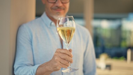 Senior man drinking glass of champagne, celebrating success. Sophisticated wine tasting by expert taster. Mid adult male relaxing with alcoholic drink outdoors on restaurant terrace or garden.
