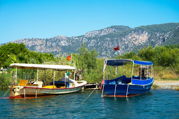 Naklejka premium Pleasure boats at pier under flag of Turkey on Dalyan River, Turkey on sunny clear summer day. Concept of water travel and the Mediterranean climate. River or water landscape