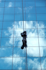 Worker cleaning mirrored windows with a reflection of the sky and clouds of a commercial building in S&atilde;o Paulo, Brazil.