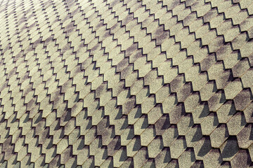 A close-up of a roof showcases a repeating geometric pattern of shingles, casting dynamic shadows that add depth and texture to the surface.