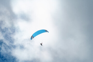 Paraglider soaring high in the sky with a yellow canopy, under a bright sun and scattered clouds.