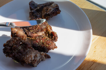 Close-up of cooked, seasoned meat on a white plate with a knife placed beside it, capturing the texture and details of the dish.
