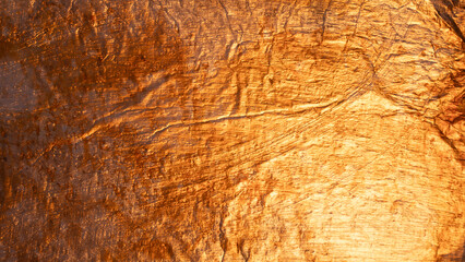 Closeup of crumpled gold foil reflecting light and creating an uneven, textured surface