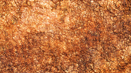 Abstract and textured background created by crumpled copper foil reflecting golden light