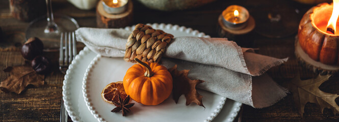 Cozy festive holiday table decor, home family Thanksgiving dinner. Traditional event, elegant natural rustic decoration. Countryside style. Burning candles, floral centrepiece pumpkin banner