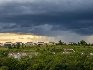 Naklejka premium Dramatic storm clouds hanging over a US residential neighborhood with bright gap in the sky on a summer evening.
