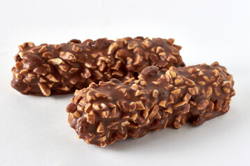 Two candy bars covered with peanuts and chocolate on a white table