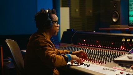 Audio designer leveling sound on a mixer control desk, professional music studio concept. Producer turns up volume and adding effects on a mixing console, recording live tracks. Camera A.