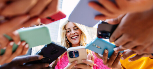 Low angle view of happy millennial people using smart phone devices together at city street. Technology lifestyle and social media concept.
