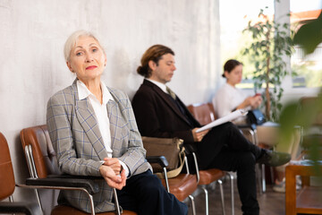 Elderly woman in business suit waiting on chair in office space