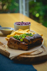 Close-up of a grilled meat slice garnished with green onions, served with potato wedges, coleslaw, and dipping sauce on a wooden board. Rustic, hearty comfort food.