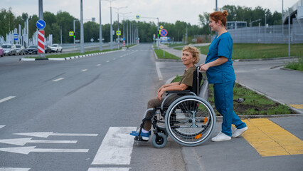 Red-haired nurse pushing an elderly woman in a wheelchair across the road. 