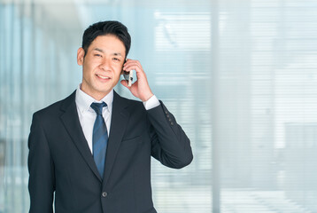 オフィスビルの前でスマホで通話するアジア人中年男性ビジネスマン
