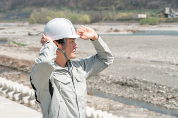 土木業・河川工事・建設現場に立つヘルメットを被った作業着姿のアジア人男性作業員
